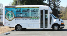 Side view of Blue Lake Rancheria bus: white van with image of Rancheria seal and fish in water on side of van.